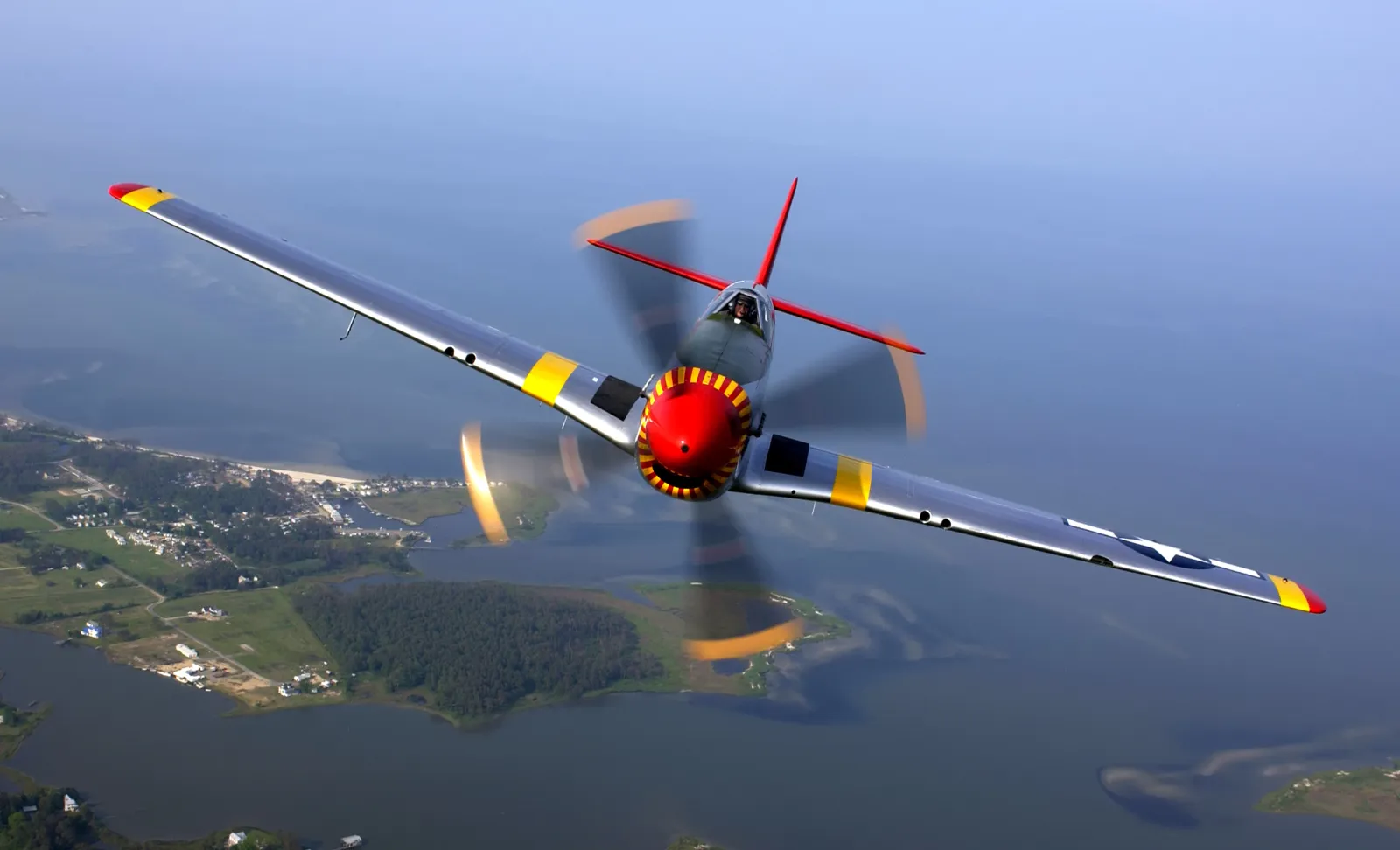 P-51D Mustang fighter aircraft in flight with distinctive bubble canopy and checkered nose art